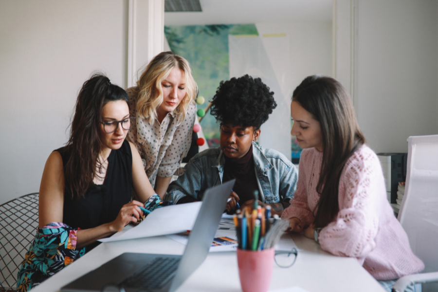 Four women gather around a table to work on a business project.