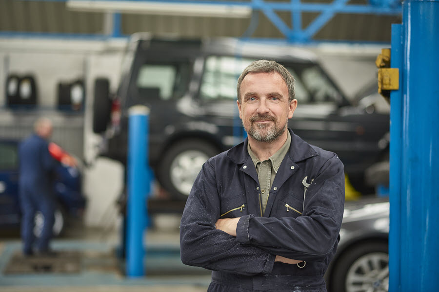 A man who is a mechanic smiling with crossed arms in an auto repair shop