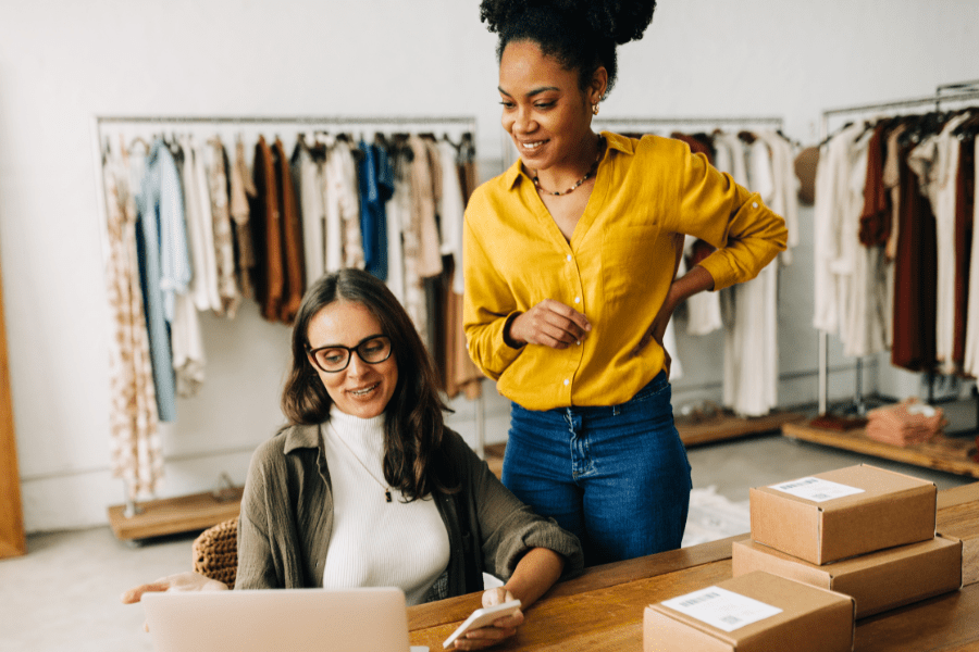 Two women in a retail clothes shop looking at a laptop.